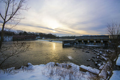 Bridge over frozen river against sky during sunset