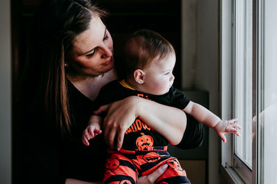 Smiling mother holding daughter sitting by window at home