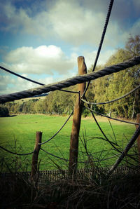 Barbed wire fence on grassy field against sky