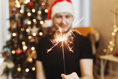 Man in red santa hat holding christmas or new year sparkler lights person