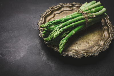 Fresh green asparagus sprouts on a round copper plate, black background. view from above