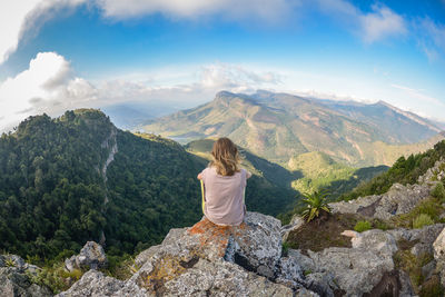 Rear view of woman sitting on rock against sky