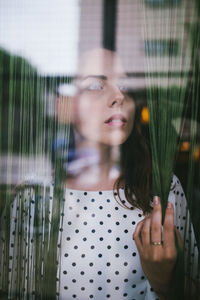 Portrait of young woman looking through window