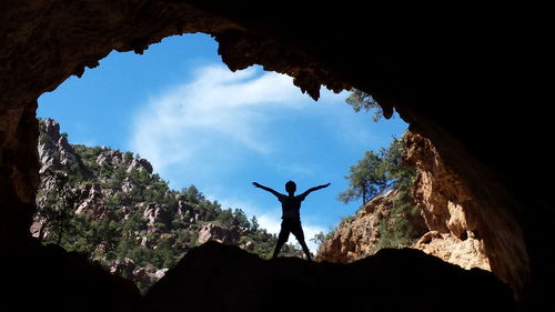 Silhouette boy with arms outstretched seen through cave