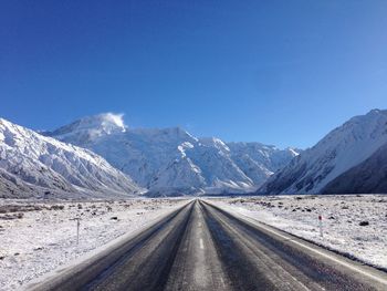 Road amidst snowcapped mountains against clear blue sky