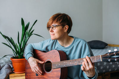Woman with short hair enjoys playing guitar at home. music lessons for adults