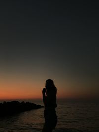 Silhouette woman standing by sea against sky during sunset