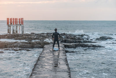 Man standing on rock at beach against sky