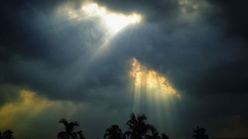 Low angle view of sun streaming through clouds in sky