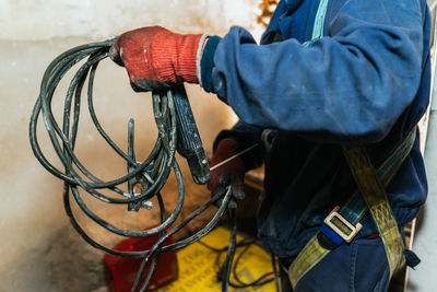 Closeup of a worker in a blue uniform, red gloves and a harness holding a dirty black cable