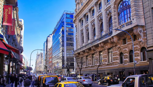 Vehicles on city street by buildings against sky