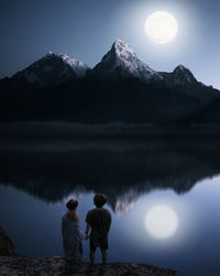 Rear view of people on mountain by lake against sky