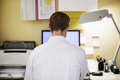 Rear view of mid adult male doctor using computer in clinic