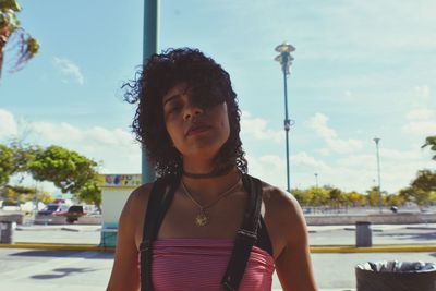 Portrait of beautiful young woman with curly hair against sky