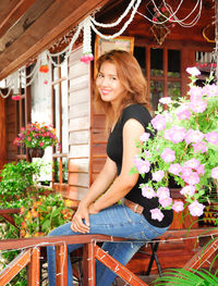 Portrait of young woman sitting on railing at porch
