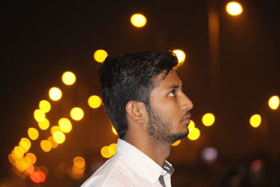 Side view of thoughtful man against illuminated light in city at night