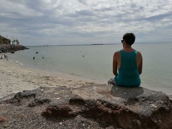 Rear view of man sitting on rock at beach