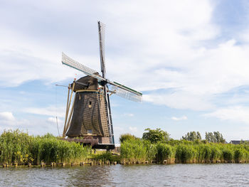 Traditional windmill by lake against sky