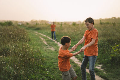 Funny boys brothers in a orange t-shirt playing outdoors on the field at sunset