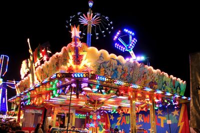 Low angle view of illuminated carousel against sky at night