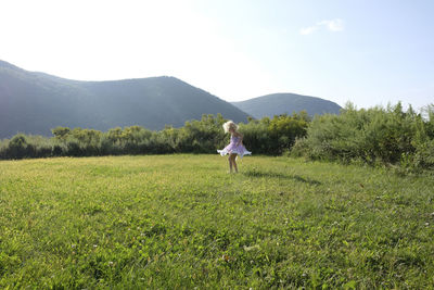 Playful girl spinning on grassy field against mountains and sky