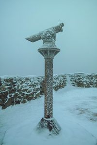 Snow covered cross against sky during winter