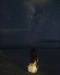 Rear view of woman sitting against sky at night