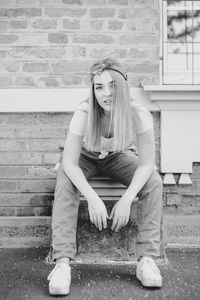 Full length of young woman sitting against wall