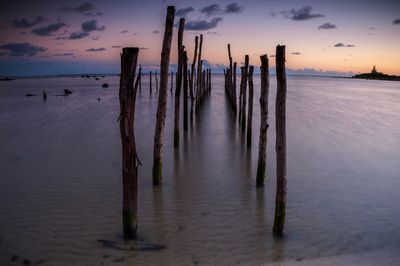 Wooden posts on beach against sky during sunset