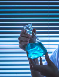 Close-up of scientist holding conical flask against blinds