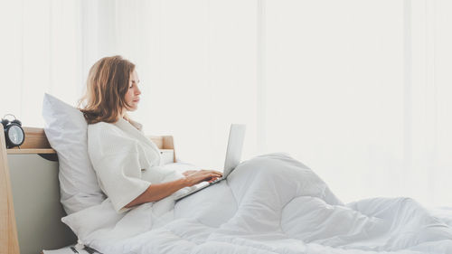 Young woman using mobile phone while sitting on bed at home