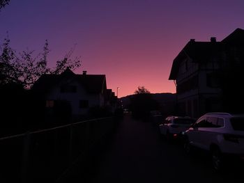 Cars on street amidst silhouette buildings against sky at sunset