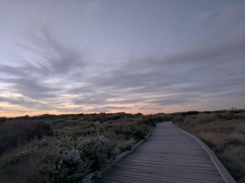 Boardwalk leading towards landscape against sky during sunset