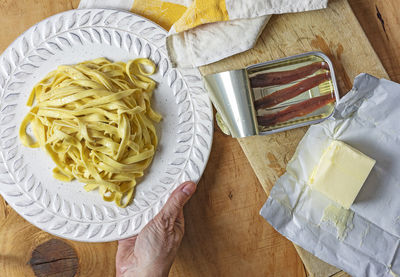 A female hand holds out a plate of fettuccine pasta seasoned with butter and cantabrian anchovies.