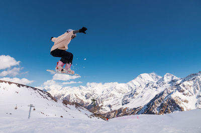 Low angle view of man skiing on snowcapped mountain against clear blue sky