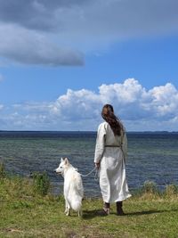 Rear view of woman with dog standing on lakeshore