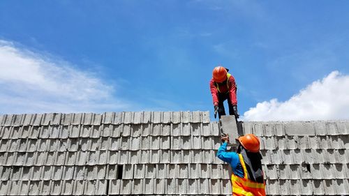 Low angle view of man working against blue sky