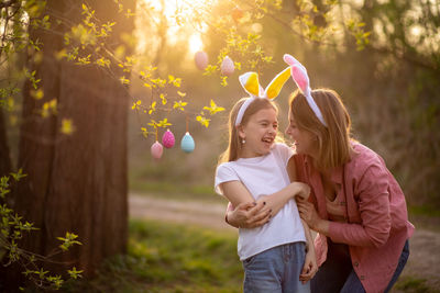 Mother and daughter standing by hanging easter eggs on branch at park