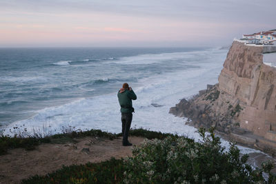 Rear view of man standing on rock by sea against sky