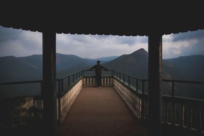 Man standing at lookout tower against mountain range