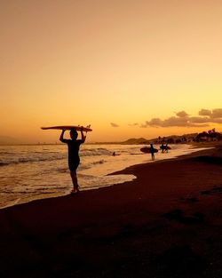 Silhouette man standing on beach against sky during sunset