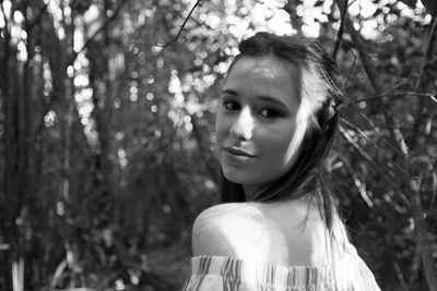 Portrait of young woman standing against trees in forest