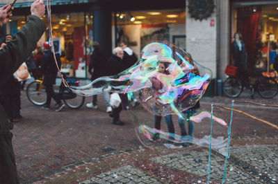 Cropped image of man making oversized bubbles on city street