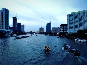 Boats in river amidst buildings in city against sky