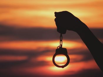 Close-up of silhouette person with handcuffs against sky during sunset