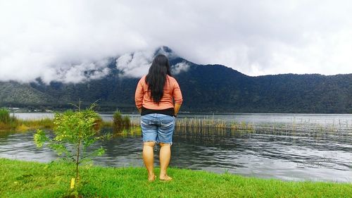 Rear view of woman standing by lake against sky