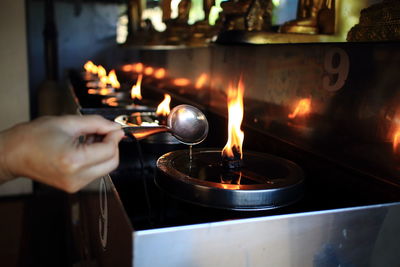 Cropped hand pouring oil in lit diya at temple