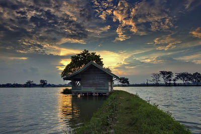 House by lake against sky during sunset