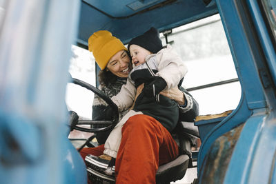 Cheerful mother with daughter sitting in tractor during winter