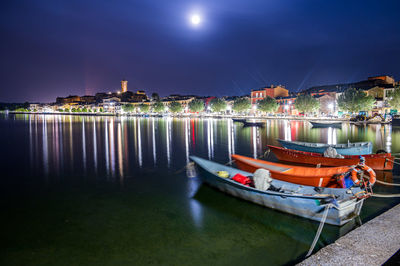 Boats moored in river against illuminated city at night